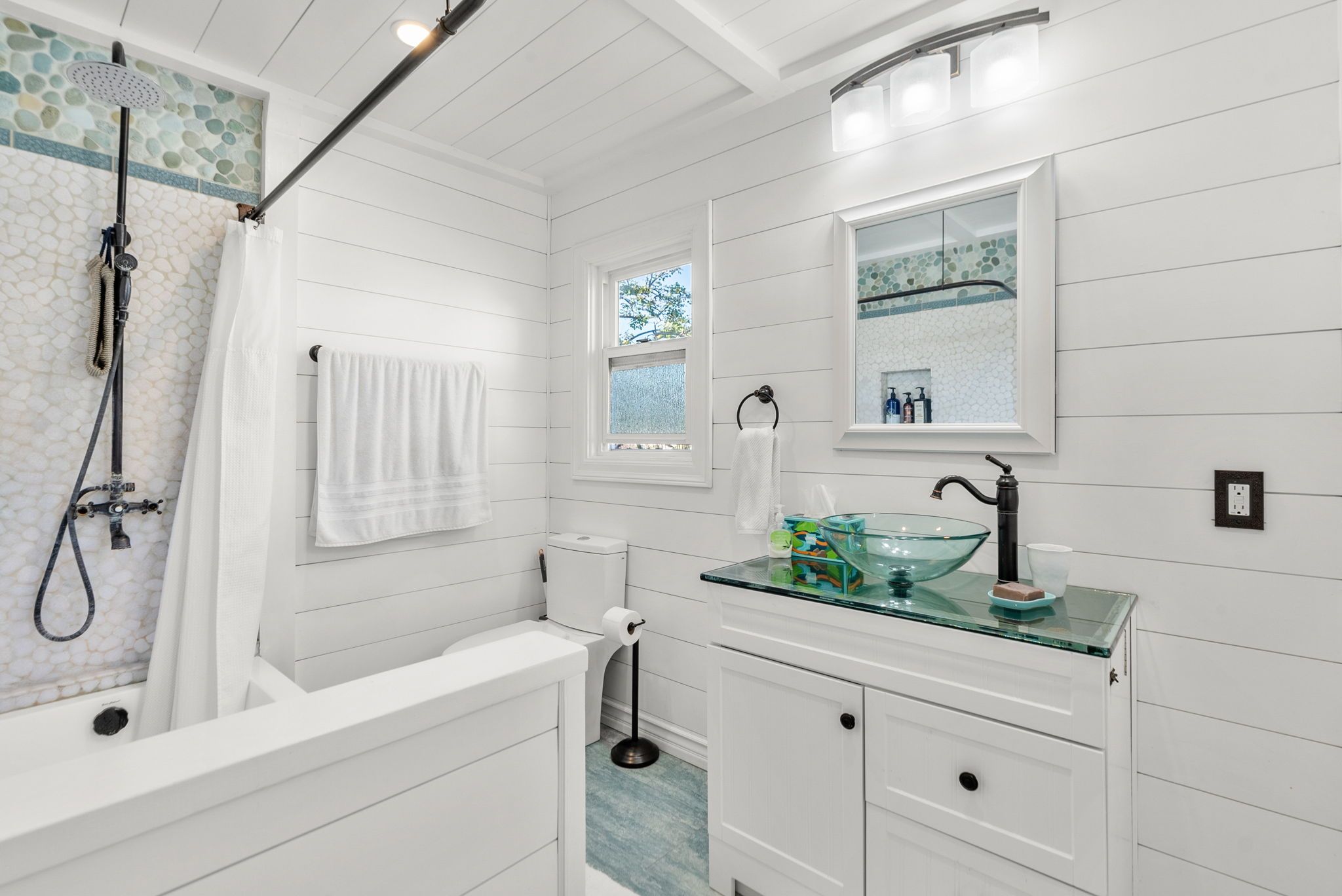 Bathroom with a shiplap wall, tub, and glass sink