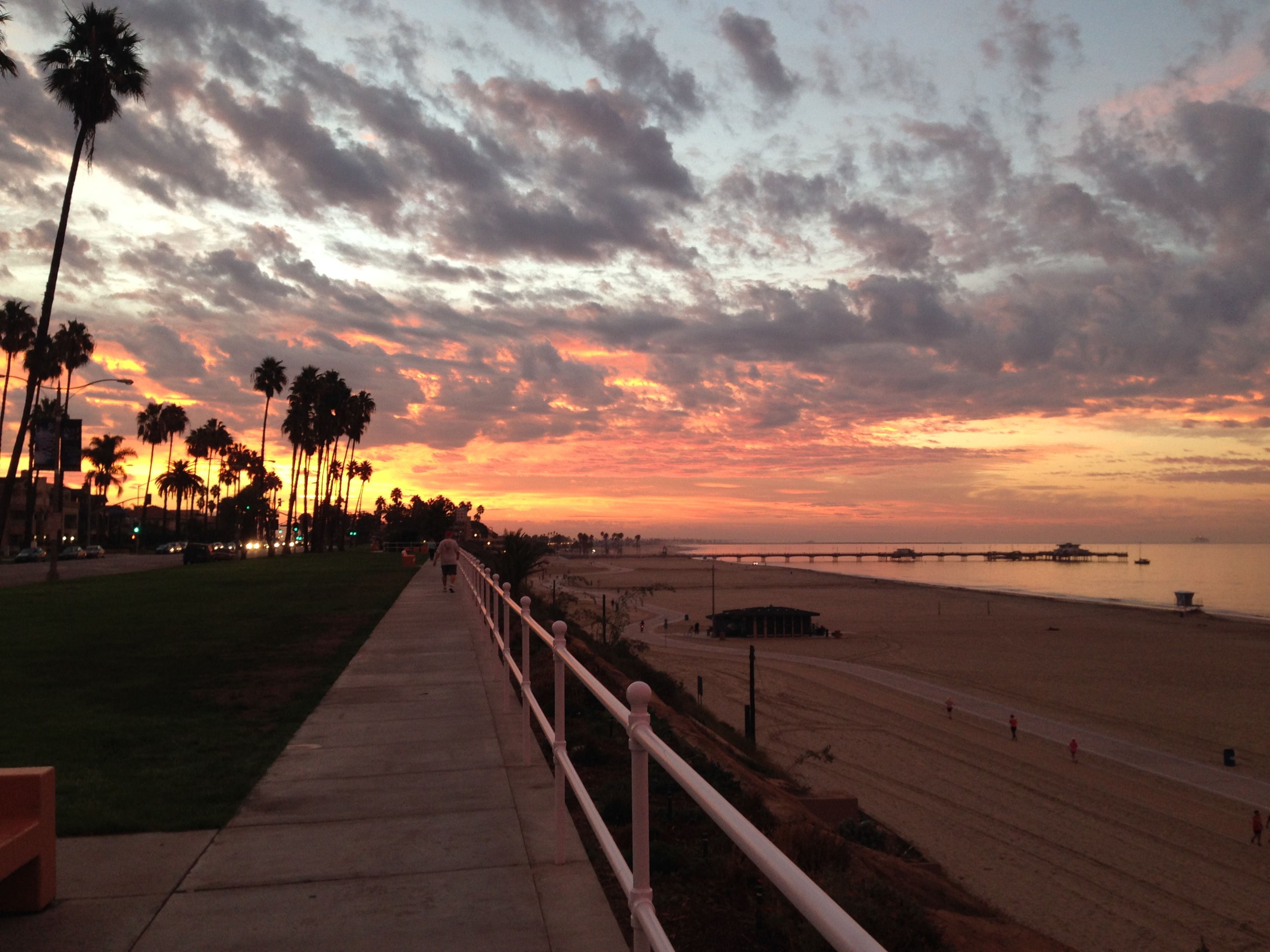 The Bluff Park path at sunset: white railing, palms, the beach below, and the pier in the distance